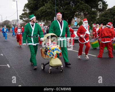 Deux hommes habillés en Père Noël pousser un enfant dans une poussette pendant la Santa fun run à Portsmouth, Angleterre Banque D'Images