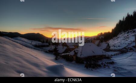 Coucher du soleil sur l'hiver village de Fundata. Paysage de montagne avec des maisons couvertes de neige dans les Carpates, Roumanie Banque D'Images