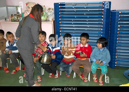 Les jeunes élèves reçoivent de l'eau chaude pour les nouilles dans une école primaire, à Da Lat, Vietnam. Banque D'Images