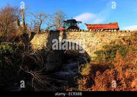 Tracteur avec remorque crossing over vieux pont de pierre avec de l'eau qui coule en dessous du ruisseau, comté de Donegal, en République d'Irlande, Europe. Décembre 2014 Banque D'Images