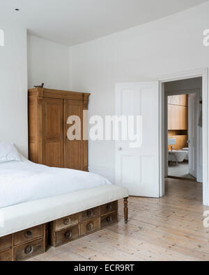 Grand lit blanc dans un minimum d'une chambre avec armoire en bois blanc et voir jusqu'à la salle de bains Banque D'Images