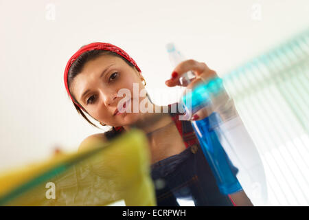 Young hispanic woman at home, travaux domestiques et d'entretien ménager, essuyage table en verre dans la salle de séjour Banque D'Images