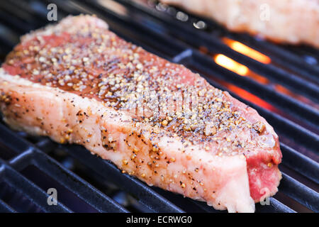 Un parfait un pouce d'épaisseur New York contre-filet de bœuf assaisonné, et au-dessus de la flamme de cuisson sur le barbecue Banque D'Images