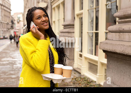 Jeune femme faisant un appel téléphonique avec le café à emporter. Banque D'Images