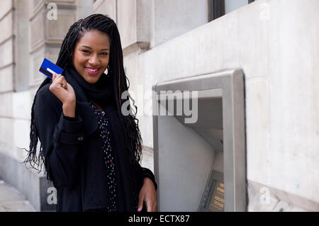 Une jeune femme tenant une carte de paiement à un distributeur mashine. Banque D'Images