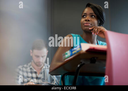 University Student sitting at desk with hand on chin Banque D'Images