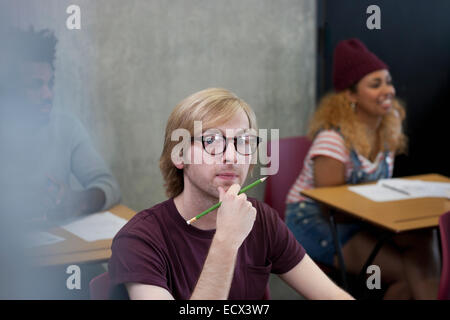 Portrait d'étudiant universitaire sitting at desk with hand on chin Banque D'Images