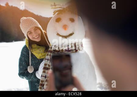 Man photographing woman with snowman Banque D'Images