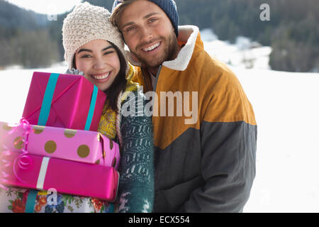 Portrait of smiling couple with Christmas gifts in snow Banque D'Images