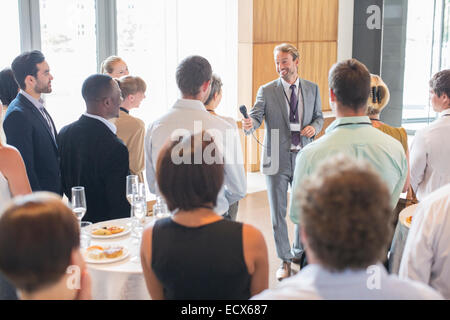Portrait of smiling man standing dans la salle de conférence, offrant du micro pour personne en audience Banque D'Images