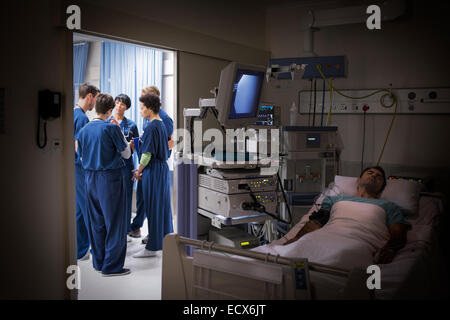 Au lit du patient en unité de soins intensifs, team of doctors discussing in background Banque D'Images