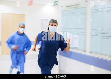 Le personnel médical portant des gommages et masques chirurgicaux rushing down hospital corridor Banque D'Images