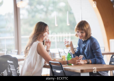 Businesswomen using cell phone in cafeteria Banque D'Images