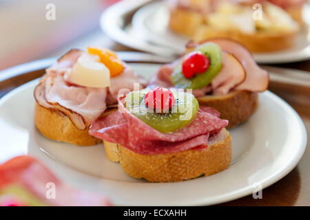 Des sandwichs au jambon, salami, orange et kiwi sur une plaque Banque D'Images