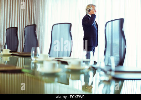 Businessman de fenêtre et à l'aide de téléphone mobile dans la salle de conférence Banque D'Images