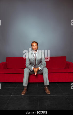 Portrait of businessman wearing costume gris assis avec les mains jointes dans une pièce sombre Banque D'Images