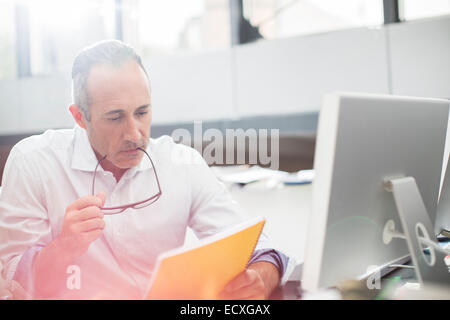 Businessman reading paperwork at office desk Banque D'Images