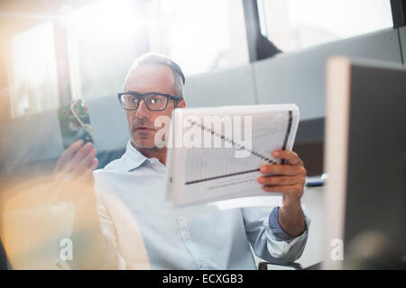 Businessman reading paperwork et cell phone in office Banque D'Images