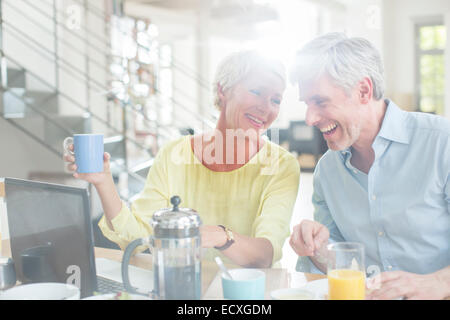 Vieux couple laughing at breakfast table with laptop Banque D'Images