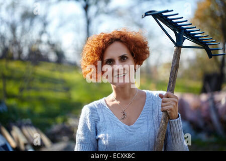 Caucasian farmer femme avec un râteau de jardin nettoyer ses feuilles tombées Banque D'Images