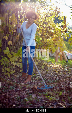 Caucasian farmer femme avec un râteau de jardin nettoyer ses feuilles tombées Banque D'Images