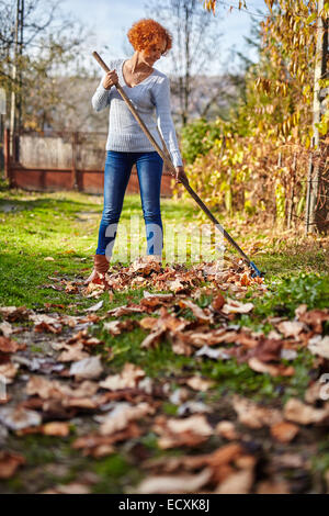 Caucasian farmer femme avec un râteau de jardin nettoyer ses feuilles tombées Banque D'Images