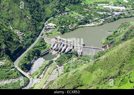 Une photographie aérienne montre un grand barrage hydroélectrique en béton enjambant une large rivière dans une vallée de montagne luxuriante et verdoyante. Le barrage comporte de multiples vannes de déversoir et est entouré de forêts escarpées Banque D'Images