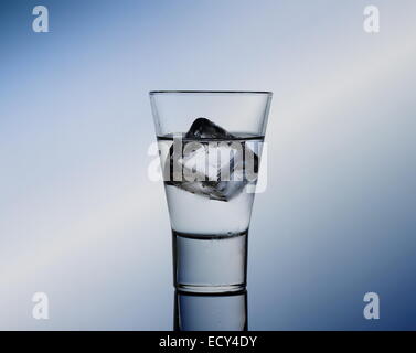 Peu de verre avec un liquide clair et des cubes de glace, fond bleu Banque D'Images