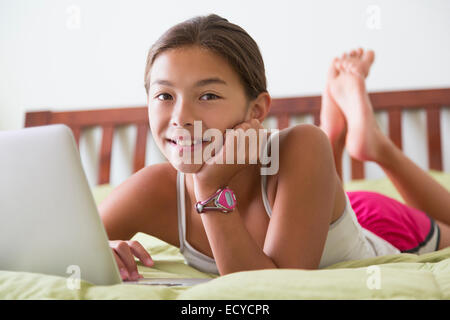 Mixed Race girl using laptop on bed Banque D'Images