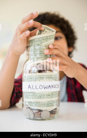 Mixed Race boy putting indemnité savings jar Banque D'Images