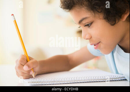 Mixed Race boy writing in notebook Banque D'Images