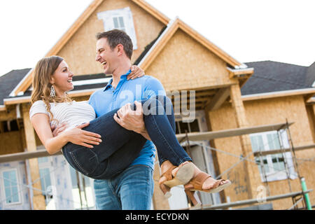 Caucasian man carrying woman près de la maison en construction Banque D'Images