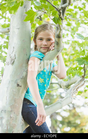 Smiling Caucasian girl climbing tree outdoors Banque D'Images