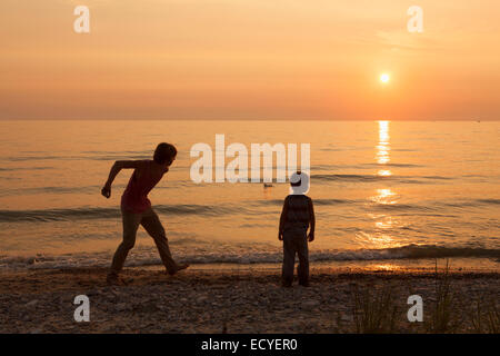 Frères de race blanche jouant sur la plage au coucher du soleil Banque D'Images