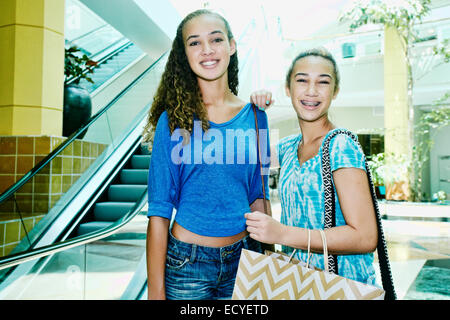 Mixed Race teenage girls shopping au centre commercial près de l'escalator Banque D'Images