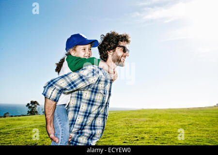 Father carrying daughter piggyback in grassy field Banque D'Images