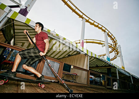 Caucasian man skateboarding avec palettes de pôle à amusement park Banque D'Images