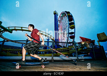 Caucasian man skateboarding avec palettes de pôle à amusement park Banque D'Images