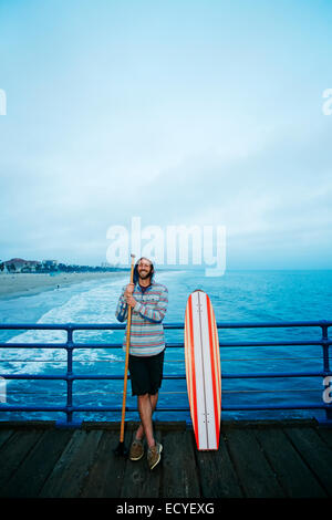 Caucasian man standing with skateboard et palette pole sur boardwalk Banque D'Images