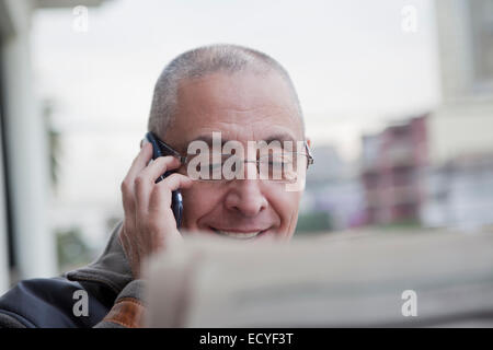 Hispanic senior man talking on cell phone and reading newspaper Banque D'Images