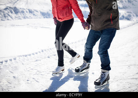 Caucasian couple patinage sur glace d'un lac enneigé Banque D'Images