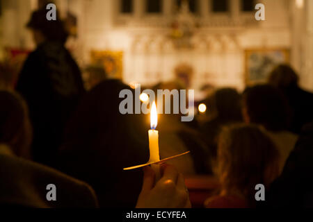 L'une 1 seule bougie flamme lumière solitaire au cours d'une Église chrétienne éclairée aux chandelles / Masse service carol & congrégation paroissiens UK Banque D'Images