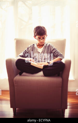 Mixed Race boy reading book in armchair Banque D'Images