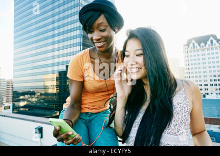 Les femmes à l'écoute des écouteurs on urban rooftop Banque D'Images