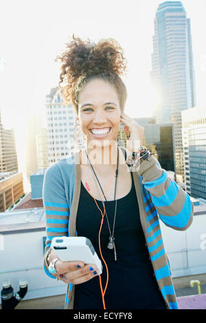 Mixed Race woman listening to écouteurs on urban rooftop Banque D'Images