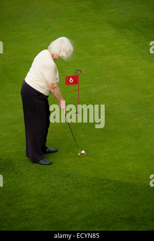 A senior woman, retraité, retraité, en vacances locations sur le vert mettre playing miniature golf, UK Banque D'Images