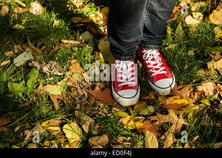 Woman in red sneakers debout dans les feuilles d'automne Banque D'Images