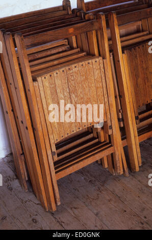 Chaises pliantes en bois empilés dans deux rangées contre mur blanc sur du plancher en bois Banque D'Images