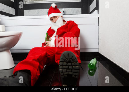 Drunken santa claus dormir à la salle de bains privative avec une bouteille de bière à la main après Sylvester Party Banque D'Images