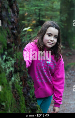 Jeune fille à la recherche de derrière un gros arbre dans une forêt pluviale tempérée Banque D'Images